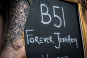 arm with tattoos and two silver welded bracelets in front of a chalkboard sign that reads "B51 Forever Jewellery"